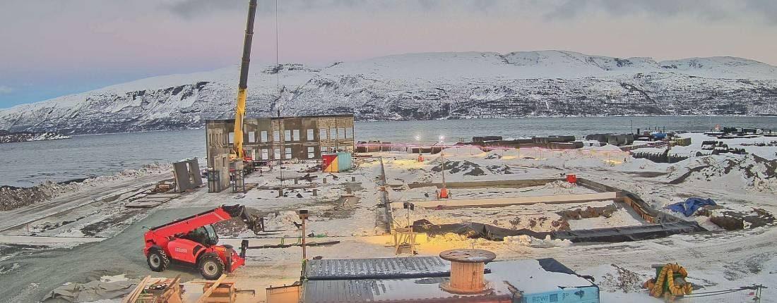 Byggeplass ved fjorden med snødekte fjell, morgenlys