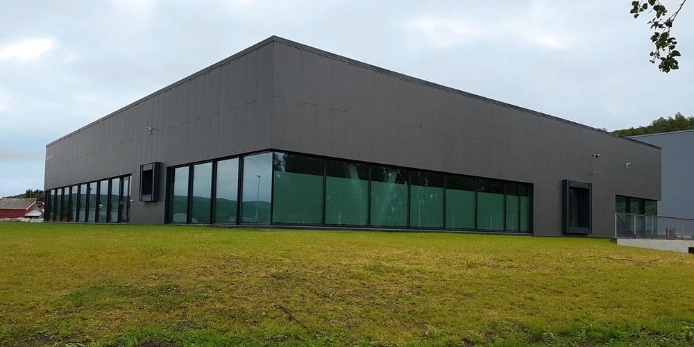 Stor hall med mørk fasade og glassvegg mot plenen