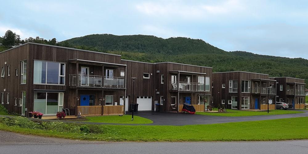 Boligblokker i mørkt tre med balkonger, skogkledd ås bak