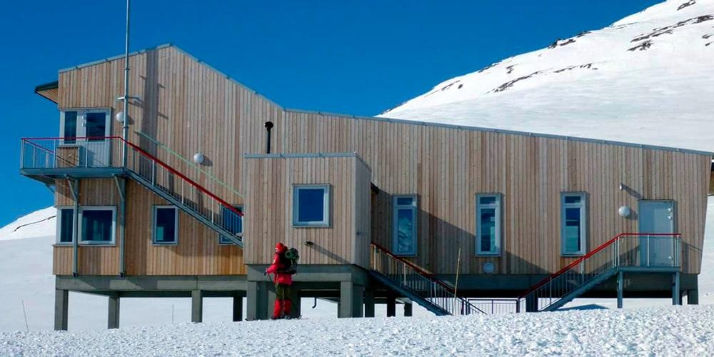 Bygg kledd i ubehandlet tre med utvendig trapp, snø og fjell bak